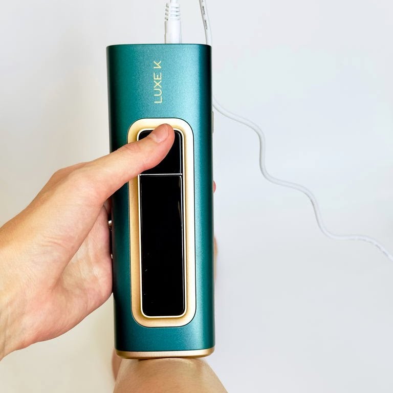 Hand holding a teal and gold electronic device with 'LUXE K' branding on a light background